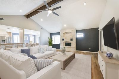 This modern, open-concept living area features a stone fireplace and high ceilings with exposed wooden beams. The space is well-lit, creating a welcoming atmosphere. | Image 2