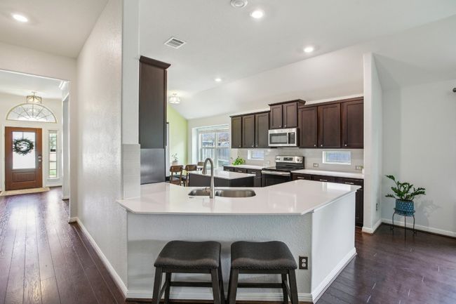Kitchen featuring a sink, dark wood-style flooring, visible vents, dark brown cabinetry, and appliances with stainless steel finishes | Image 11