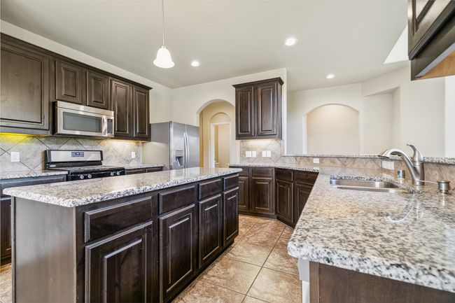 Kitchen featuring appliances with stainless steel finishes, a sink, a center island, arched walkways, and dark brown cabinets | Image 11
