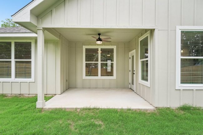 View of exterior entry featuring a patio, a yard, board and batten siding, and ceiling fan | Image 35