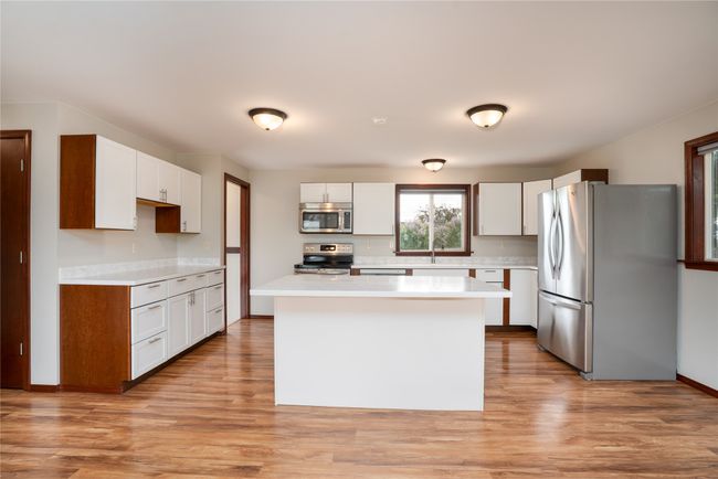 Kitchen with appliances with stainless steel finishes, light countertops, a center island, and light wood-type flooring | Image 12
