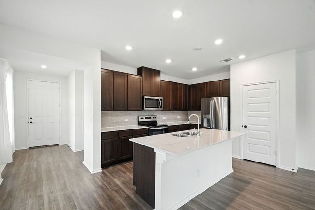 Kitchen with dark brown cabinets, tasteful backsplash, appliances with stainless steel finishes, a center island with sink, and recessed lighting | Image 5