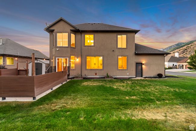 Back of property at dusk featuring stucco siding, a yard, a shingled roof, and a storage shed | Image 41
