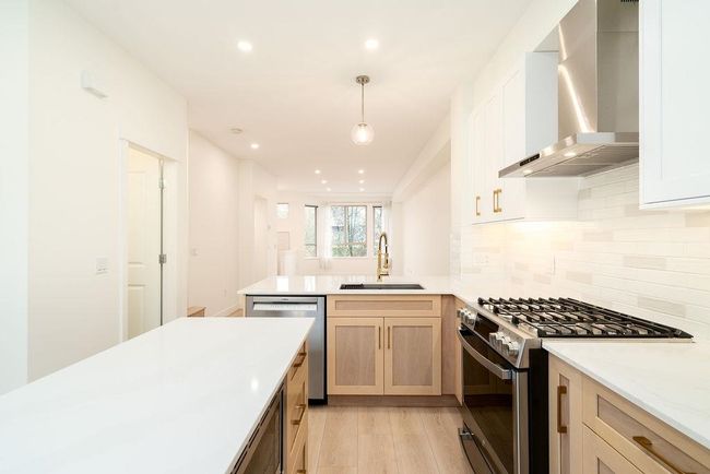 Kitchen featuring light countertops, a sink, stainless steel appliances, wall chimney range hood, and decorative backsplash | Image 5
