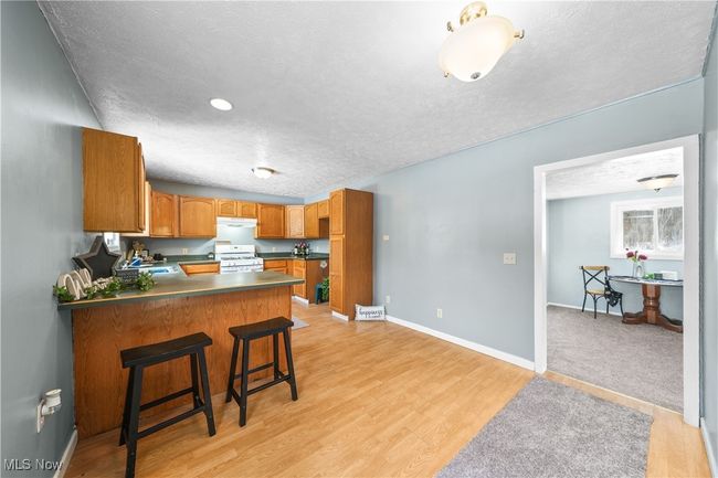 Kitchen featuring a kitchen breakfast bar, gas range gas stove, light hardwood / wood-style floors, kitchen peninsula, and a textured ceiling | Image 7