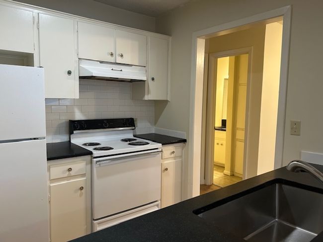 Kitchen featuring a sink, under cabinet range hood, white appliances, dark countertops, and white cabinets | Image 6
