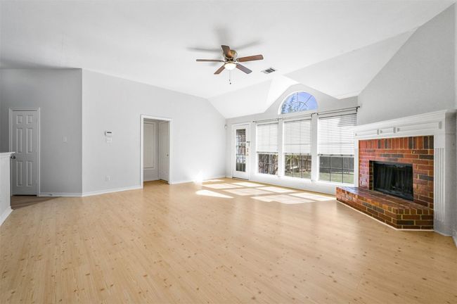 Unfurnished living room featuring a ceiling fan, light wood finished floors, a brick fireplace, and lofted ceiling | Image 6