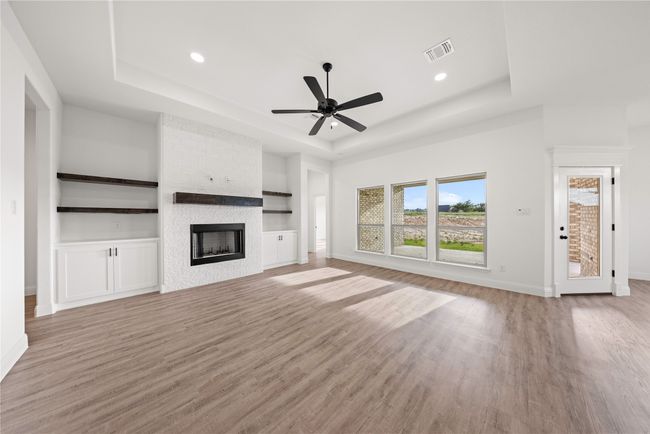 Unfurnished living room with a raised ceiling, light wood finished floors, ceiling fan, baseboards, and a fireplace | Image 11