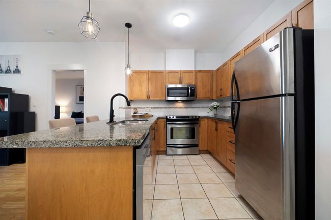 Kitchen with a sink, decorative light fixtures, a peninsula, brown cabinetry, and appliances with stainless steel finishes | Image 5
