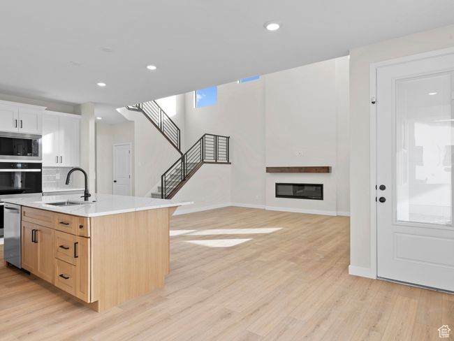 Kitchen featuring light wood finished floors, a glass covered fireplace, an island with sink, appliances with stainless steel finishes, and a sink | Image 12