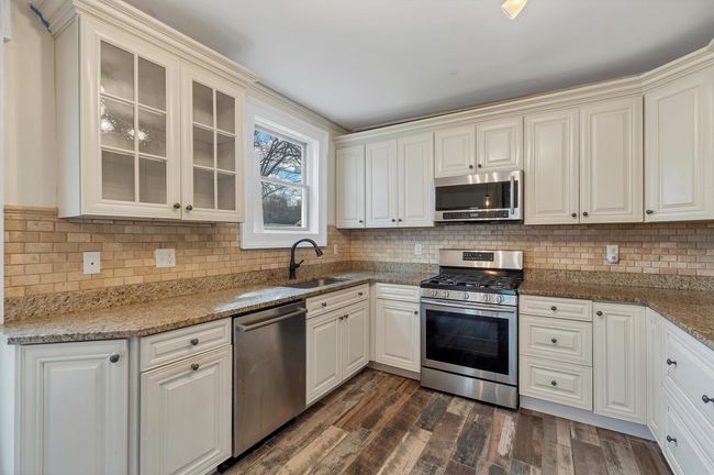 Kitchen featuring appliances with stainless steel finishes, a sink, glass insert cabinets, dark wood finished floors, and decorative backsplash | Image 14