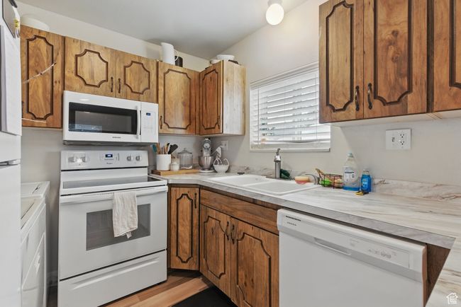 Kitchen with light countertops, brown cabinets, a sink, and white appliances | Image 8
