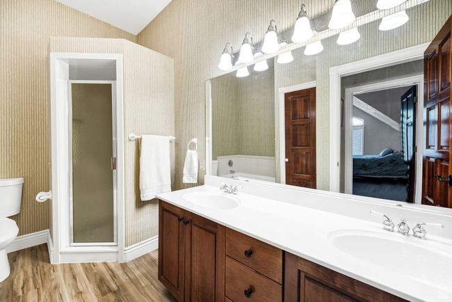 Ensuite bathroom featuring wallpapered walls, wood finished floors, double vanity, a garden tub, and a shower stall | Image 55