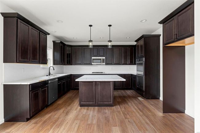 Kitchen with hardwood / wood-style floors, decorative light fixtures, a kitchen island, dark brown cabinetry, and stainless steel appliances | Image 24