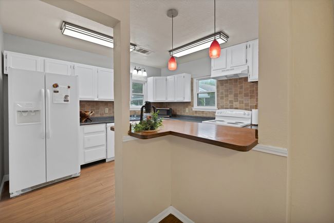 Kitchen featuring granite countertops, backsplash, bar, under cabinet range hood, white appliances, and white cabinetry | Image 12