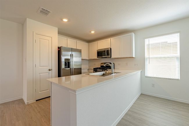Kitchen featuring appliances with stainless steel finishes, light wood-style flooring, a peninsula, baseboards, and light countertops | Image 5