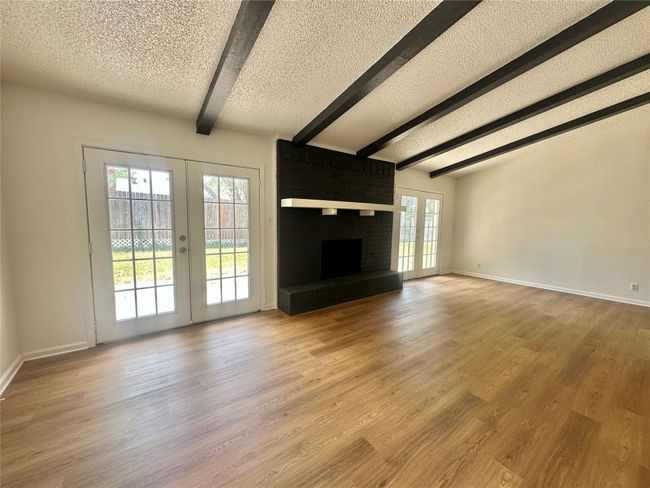 Unfurnished living room featuring french doors, beamed ceiling, wood finished floors, and a textured ceiling | Image 8