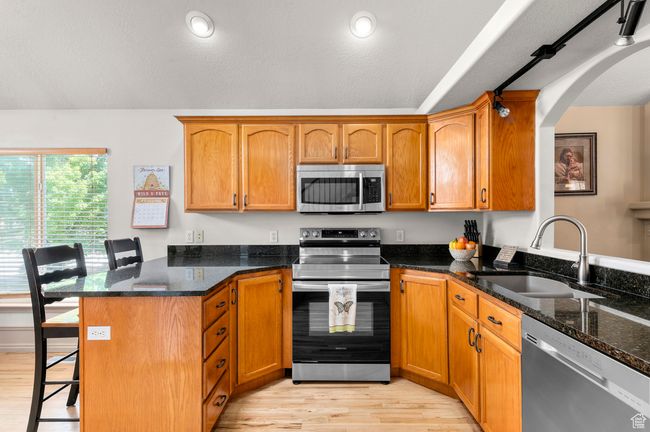 Kitchen with stainless steel appliances, a sink, a peninsula, a breakfast bar, and light wood flooring | Image 7
