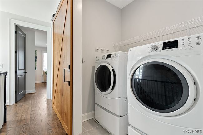 Clothes washing area featuring washing machine and clothes dryer, a barn door, wood finished floors, laundry area, and baseboards | Image 26