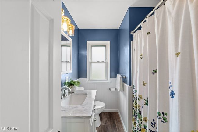 Bathroom with vanity, toilet, a wainscoted wall, wood finished floors, and a shower with shower curtain | Image 16