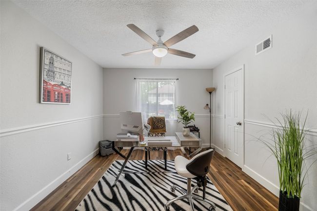 This bedroom / home office features wood flooring and neutral walls. It includes a ceiling fan, a large window providing natural light. | Image 14