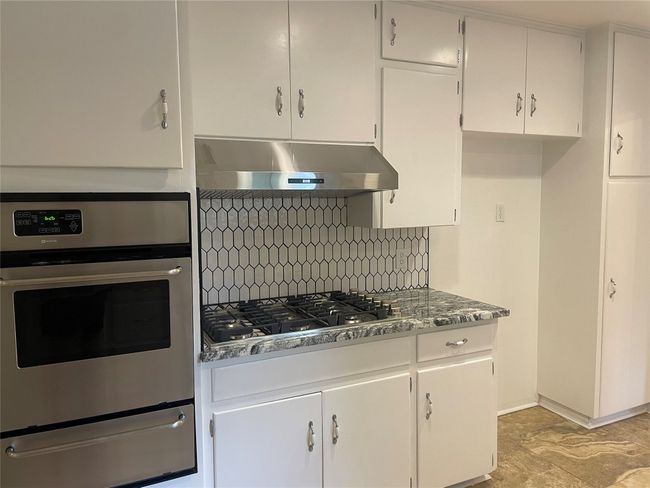 Kitchen with exhaust hood, a warming drawer, appliances with stainless steel finishes, decorative backsplash, and white cabinetry | Image 4