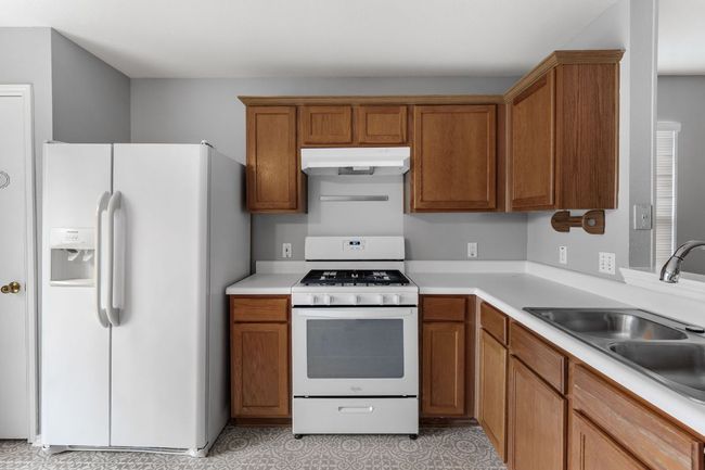 Kitchen with white appliances, light countertops, brown cabinets, under cabinet range hood, tile floor, and light floors | Image 10
