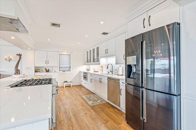 Kitchen with appliances with stainless steel finishes, light wood-style floors, white cabinets, light stone countertops, and ornamental molding | Image 7