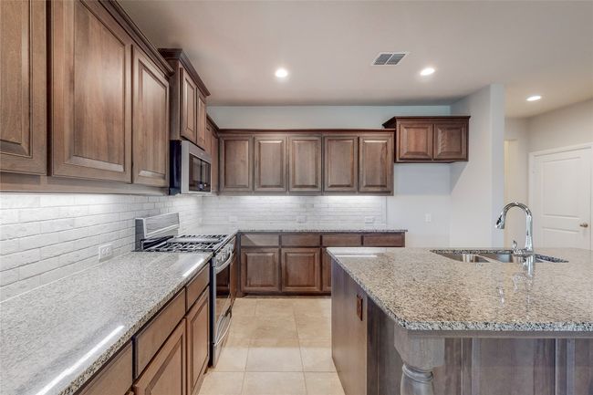 Kitchen with stainless steel appliances, a sink, backsplash, light stone counters, and recessed lighting | Image 9