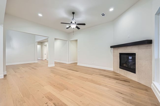 Unfurnished living room with visible vents, baseboards, a fireplace, a ceiling fan, and light wood-style floors | Image 4