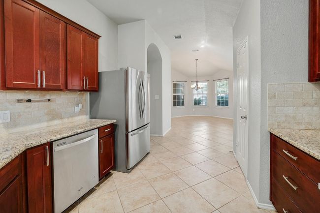 Kitchen featuring appliances with stainless steel finishes, backsplash, a chandelier, light tile patterned floors, and lofted ceiling | Image 12