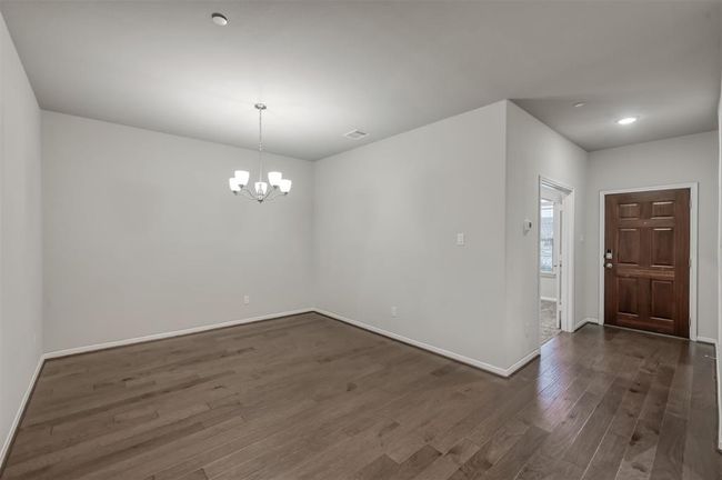 Spacious room with hardwood floors and modern lighting, adjacent to kitchen and living spaces, inviting for family gatherings. | Image 7