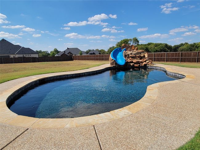 View of swimming pool featuring a fenced backyard and a water slide | Image 5
