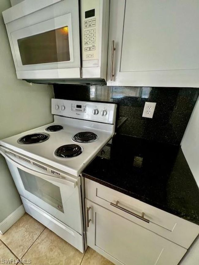 Kitchen with light tile patterned flooring, white cabinetry, white appliances, and backsplash | Image 10