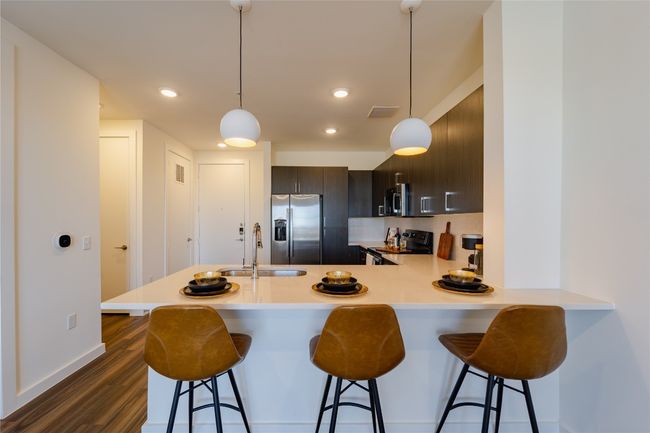 Kitchen with stainless steel appliances, light countertops, a breakfast bar, a sink, and dark wood-type flooring | Image 4
