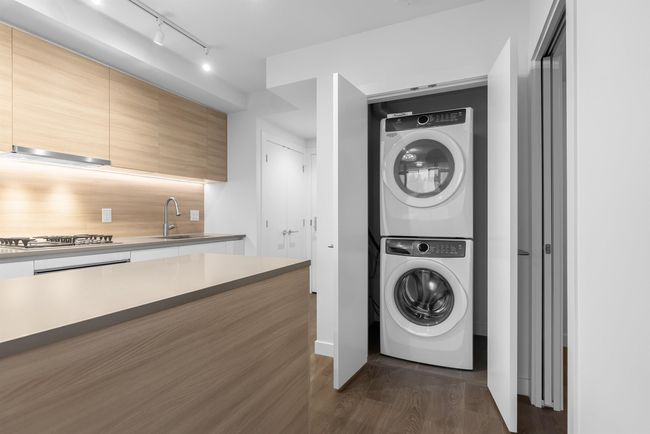 Washroom with a sink, dark wood finished floors, track lighting, stacked washing maching and dryer, and laundry area | Image 6
