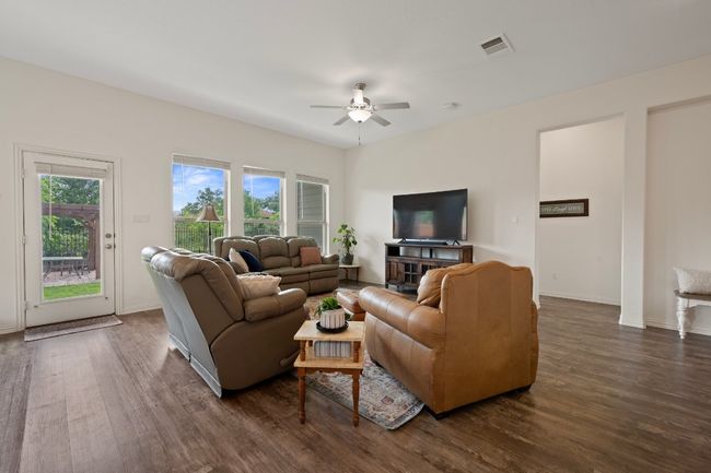 Living area with dark wood-type flooring, a ceiling fan, and baseboards | Image 11