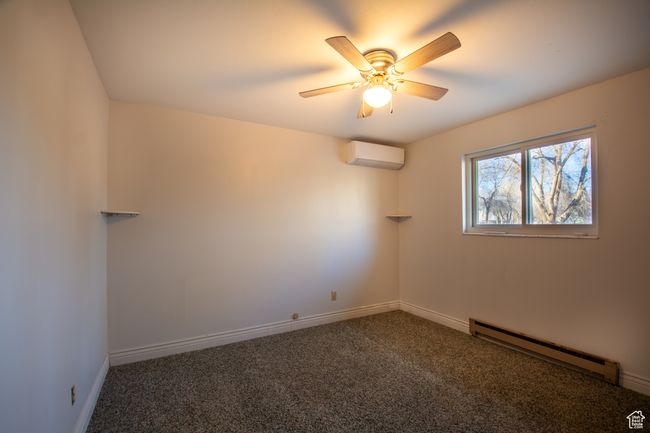 Carpeted empty room featuring baseboard heating, ceiling fan, and an AC wall unit | Image 9