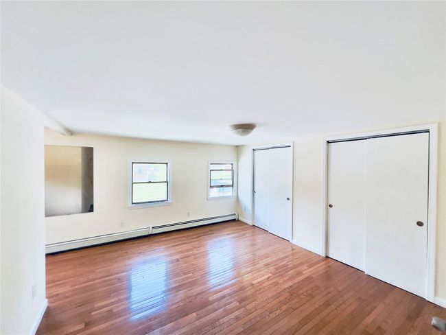 Unfurnished bedroom with baseboard heating, two closets, and hardwood / wood-style floors | Image 12