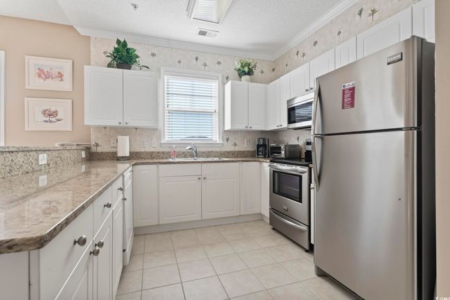 Kitchen with stainless steel appliances, a sink, white cabinets, a peninsula, and light tile patterned flooring | Image 5