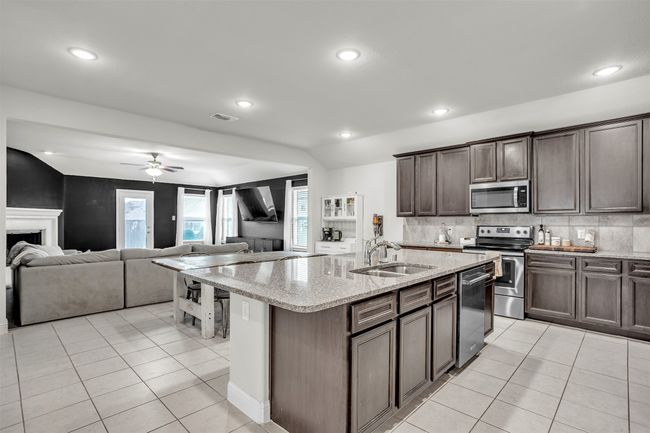 Kitchen with appliances with stainless steel finishes, light tile patterned floors, dark brown cabinets, ceiling fan, and a center island with sink | Image 7