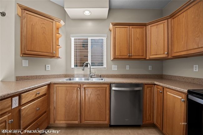 Kitchen with light countertops, stainless steel dishwasher, electric range, a sink, and brown cabinetry | Image 15