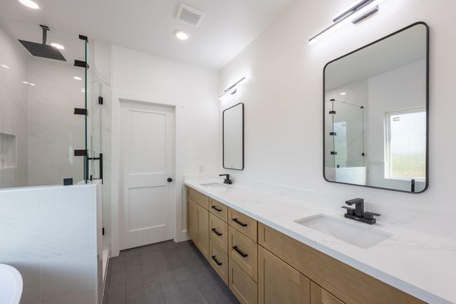Enjoy a luxurious daily routine in this spa-inspired bathroom, featuring a dual sink vanity with soft wood cabinetry, modern black fixtures, and quartz countertops. | Image 23
