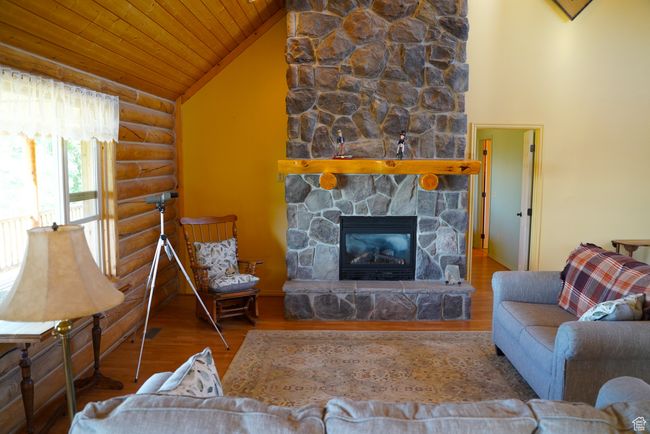 Living area featuring rustic walls, wooden ceiling, wood finished floors, a fireplace, and vaulted ceiling | Image 8
