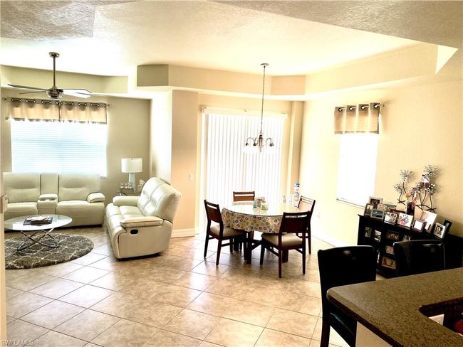 Dining space with ceiling fan with notable chandelier, light tile patterned flooring, a textured ceiling, and a healthy amount of sunlight | Image 4