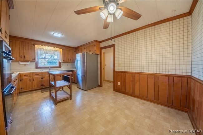 Kitchen with sink, crown molding, stainless steel fridge, ceiling fan, and wood walls | Image 14