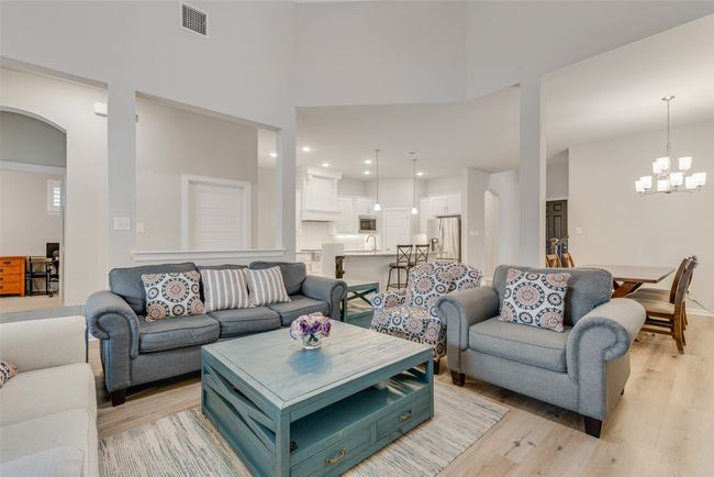 Living room featuring a high ceiling, a notable chandelier, visible vents, light wood-style flooring, and arched walkways | Image 6