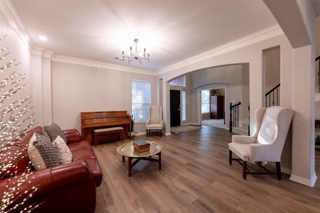 Living area featuring arched walkways, a chandelier, wood finished floors, ornamental molding, and stairs | Image 7
