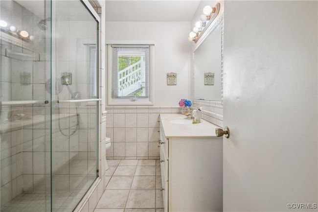 Full bathroom featuring vanity, tile walls, a shower stall, tile patterned flooring, and a wainscoted wall | Image 22