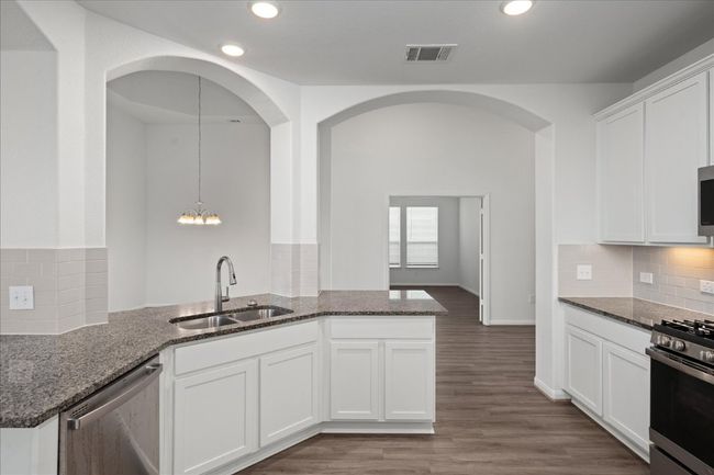 Kitchen with a sink, stainless steel appliances, dark stone countertops, a peninsula, and white cabinetry | Image 13